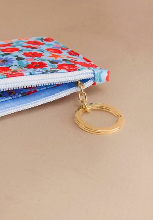 Puzdro s kvetinovým vzorom s červenými a modrými kvetmi na svetlo modrom pozadí, s zlatým prstencovým kovovým príslušenstvom a bielym zipsom.