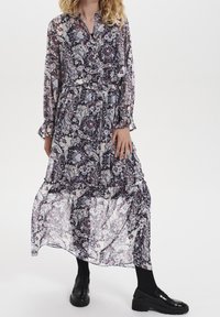 Lång, flödande klänning i lila och krämfärgad paisleymönster med långa ärmar, elastisk midja och volangdetaljer vid ärmsluten och fållen.