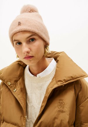 Bonnet tricoté rose clair avec un pompon et un détail de logo ; veste matelassée marron avec un col haut, dotée de matériels dorés et d'un logo en relief.