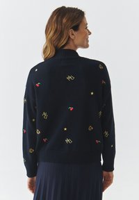 Maglione blu navy a maglia con collo a coste; decorato con ciliegie ricamate colorate, stelle e loghi in filo dorato sul retro.