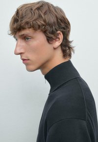 Maglione nero a collo alto in maglia con tessuto testurizzato, design aderente e colletto alto. Vista laterale che mostra i dettagli delle cuciture delle spalle.