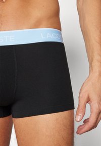 Sorte boxertruser med en lys blå elastisk midje, med tekstbranding. Glatt stoff og tettsittende design, som fremhever komfort og stil.