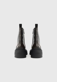 Bottines en cuir noir avec une semelle épaisse, fermeture éclair et détails élastiques au niveau du talon. Texture lisse avec un minimum de coutures.