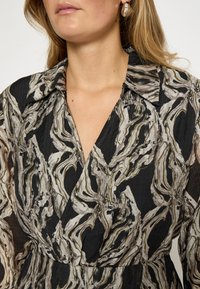 Vestido negro con un patrón abstracto giratorio en tonos crema y dorado. La tela parece ligera y de textura suave.