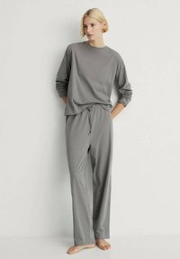 Sivý loungewear set, ktorý obsahuje uvoľnené tričko s dlhým rukávom a nohavice s elastickým pásom. Vyrobené z mäkkej tkaniny s hladkou textúrou.