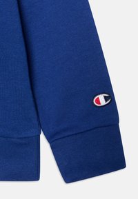 Manica di felpa blu con polsini a coste e un logo ricamato con accenti rossi e bianchi. Realizzata in un tessuto morbido e testurizzato.