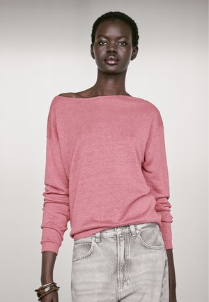 Maglione rosa chiaro, con scollatura a spalle scoperte, di taglio morbido e maniche lunghe, abbinato a jeans in denim grigio chiaro.