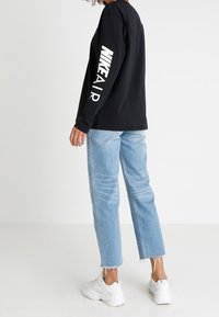 Svart långärmad t-shirt med texten "NIKE AIR" i stora vita bokstäver på ärmen, i kombination med ljusblå raka jeans och vita sneakers.