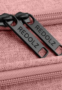 Roze textiel met een zwarte ritssluiting met het label "REDOLZ." De ritsen hebben synthetische tanden en een gladde stofrand.
