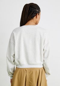 Sudadera gris claro con mangas largas y un dobladillo acanalado, vista desde atrás. La tela parece suave y ligeramente texturizada.