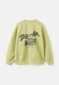 Vihreä collegepaita pyöreällä kaula-aukolla ja pitkällä hihoilla. Suuri "Discover New Heights" -grafiikka tummanharmaana. Pehmeä koostumus.