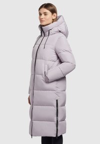 Ljuslavendelfärgad lång pufferjacka med hög huva, quiltat mönster, dragkedja fram och sidofickor. Har svarta dragkedjadekorationer.
