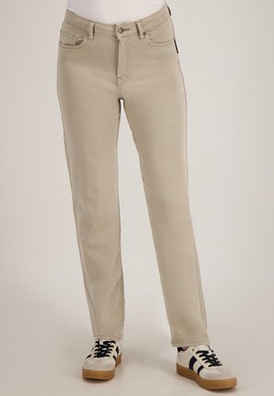 Beige rechte broek met witte sneakers met zwarte strepen en gumzolen, getoond van taille tot voeten op een neutrale achtergrond.