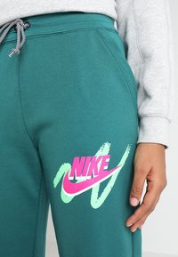 Teal sweatpants med dragsko i midjan, med en stor, djärv rosa och mintgrön Nike-logotyp med penseldrag-detajer. Mjukt tyg.