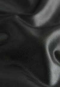 Tissu en cuir noir lisse avec une texture fine et des plis doux reflétant la lumière.