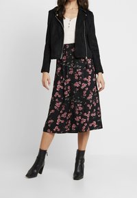 Veste de motard en daim noire sur un haut boutonnière rose et une jupe midi noire à motifs floraux avec des fleurs roses et vertes, assortie à des bottines noires.