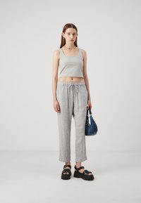 Un débardeur gris court, un pantalon à rayures gris clair avec cordon de serrage, des sandales à plateforme noires et un petit sac bleu. Tenue simple et décontractée.