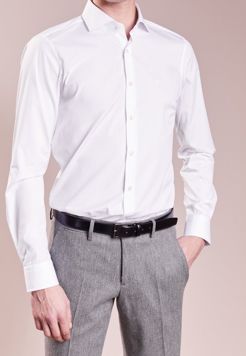 Camisa blanca de manga larga con cuello clásico, botones al frente y tejido liso, combinada con pantalones grises texturizados y cinturón negro.