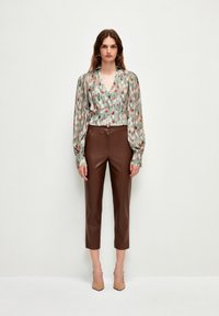Blusa a maniche lunghe, stampata in verde con accenti rosa e beige, abbinata a pantaloni in ecopelle color marrone, tagliati e a tacco nudo.