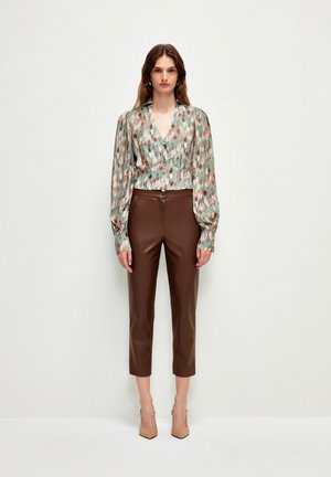 Blusa a maniche lunghe, stampata in verde con accenti rosa e beige, abbinata a pantaloni in ecopelle color marrone, tagliati e a tacco nudo.
