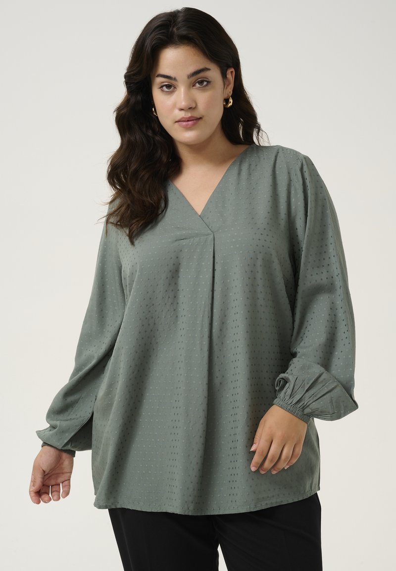 Green blouse with a V-neck, puffed long sleeves, and textured dot pattern. Made of lightweight fabric, features a relaxed fit and gathers.