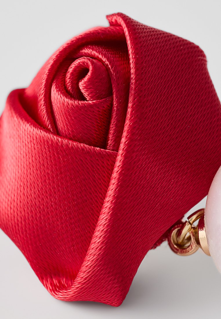 Spilla a forma di rosa in raso rosso con un design a petali a spirale e hardware color oro, dotata di un elegante perla bianca lucida.