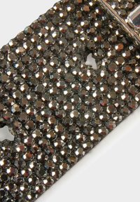 Materiale nero ricoperto di perline lucide e sfaccettate, che riflettono la luce. Presenta fori e un bordo curvato, creando una superficie texture.