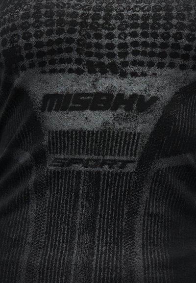 Tissu noir avec des motifs texturés et le mot "MISBHV" en lettres majuscules grasses, centré sur la surface.