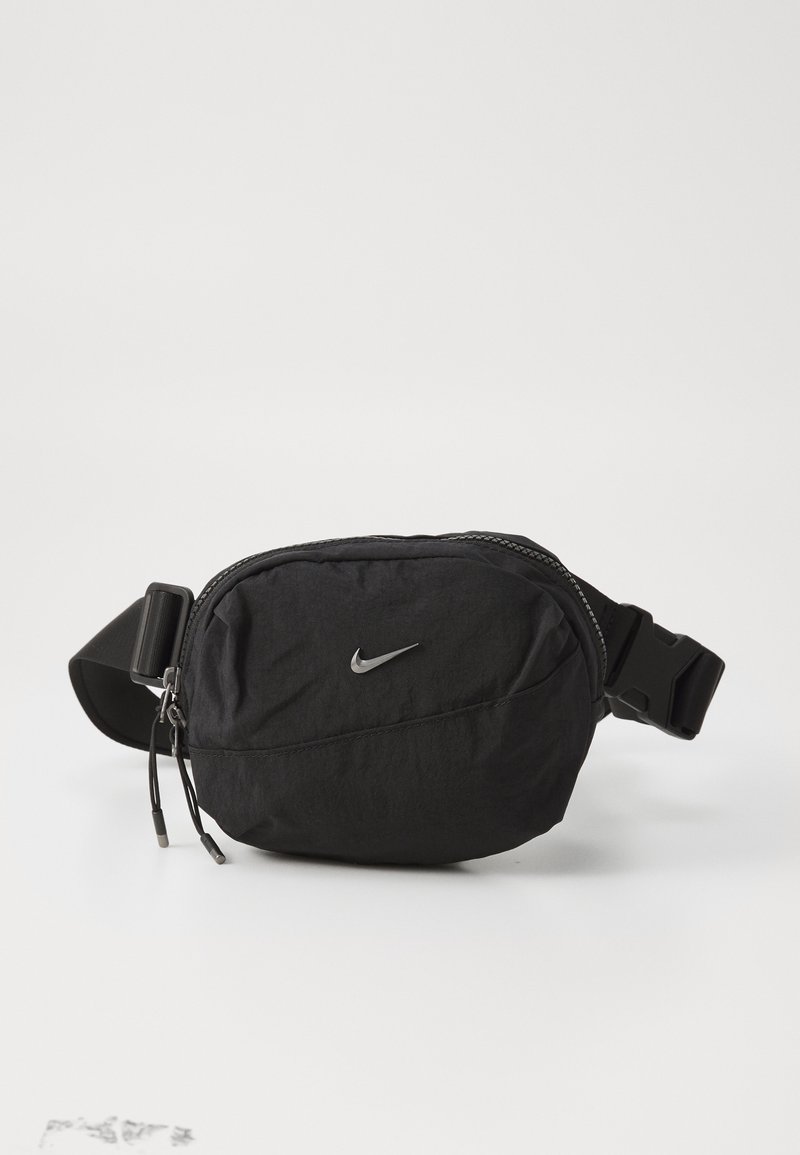 Svart Nike bauletto laget av lett stoff, med glidelås, justerbar stropp og en liten sølv logo accenten.
