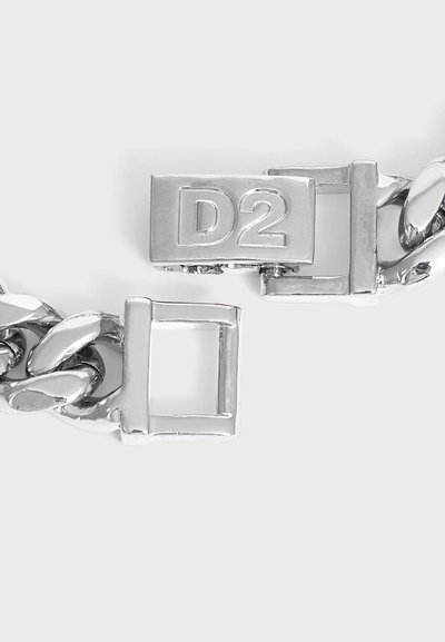 Gros plan d'un fermoir de chaîne en argent avec une serrure rectangulaire gravée de "D2" sur un fond clair.