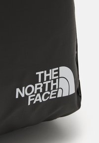 Černý látkový batoh s velkým bílým logem "THE NORTH FACE", s hladkým povrchem a zakulacenou strukturou.