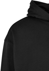 Sudadera con capucha negra hecha de un tejido suave, con una textura lisa y un corte relajado, presenta un escote curvado y costuras en los hombros.