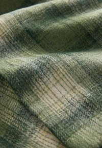 Vilnas audums ar zaļi un beigā rakstu, mīksta tekstūra un nelielas krāsas un spīduma variācijas.