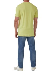 Lichte gele t-shirt met korte mouwen en een rechte snit, gecombineerd met lichtblauwe denim jeans en witte sneakers. Achteraanzicht getoond.