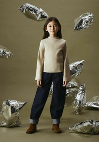 Beige ribbad långärmad topp, mörka denimvidbyxor med upprullade fållar, bruna ankelboots. Silverfärgade skrynkliga folieaccenter i bakgrunden.