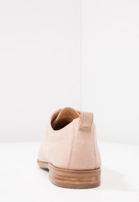 Chaussure en daim rose clair avec une texture lisse, un bout rond et un petit talon. Présente une languette arrière et des accents de couture le long des coutures.