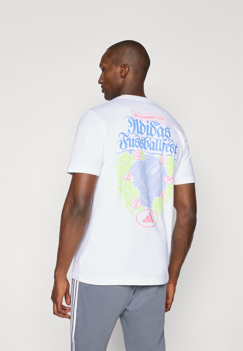 Hvid bomulds t-shirt med et farverigt grafisk motiv på ryggen, som har et fodbolddesign, tekst i blå og pink samt Adidas-logoet nederst.