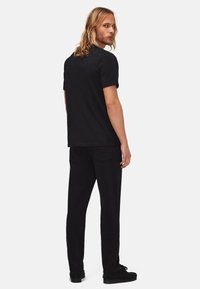 Sort bomulds t-shirt med korte ærmer og lige snit, parret med sorte bukser, der har to baglommer og en afslappet pasform.