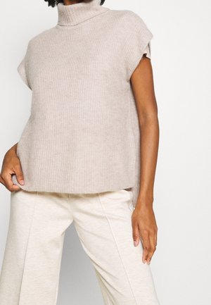 Beige knitted sleeveless turtleneck top with a relaxed fit, featuring a ribbed texture and a straight hem. Paired with light-colored pants.