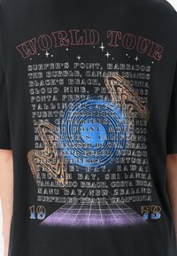Black graphic t-shirt featuring multicolored "WORLD TOUR" text and various beach names, with a circular blue design and grid pattern at the bottom.