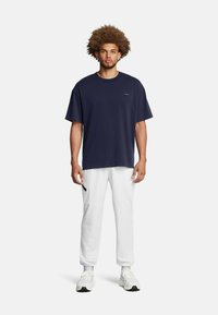 Navyblaue Baumwoll-T-Shirt mit entspanntem Schnitt, kombiniert mit weißen Jogginghosen mit Akzentreißverschluss und elastischen Bündchen.