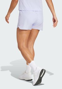 Pantalones cortos deportivos de color púrpura claro con un acabado texturizado, que presentan un diseño de abertura lateral. Combinados con zapatillas blancas y calcetas blancas acanaladas.