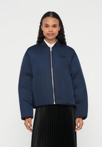 Navy blue bomber jacket with a front zipper, ribbed collar, and embroidered accent. Made from smooth fabric with a relaxed fit.