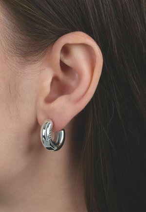 Primer plano de una oreja izquierda con cabello oscuro que lleva un arete de aro grueso y brillante de plata.