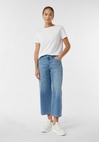 T-shirt en coton blanc associé à un jean large bleu clair. La tenue comprend des baskets blanches et un léger éclat dans le tissu en denim.