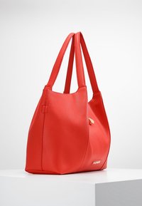 Punainen nahkainen kassi teksturoidulla pinnalla, jossa on kaksi olkahihnaa ja kultainen yksityiskohta. Yksinkertainen, tilava muotoilu, jossa on löysä muoto.