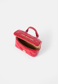 Raudona siuvinėta dirbtinės odos rankinė su auksinės spalvos užsegimu, turinti viršutinę rankeną ir iškilų "LOVE MOSCHINO" logotipą ant atlapo.
