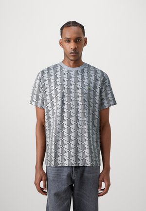 T-shirt gris à manches courtes avec un motif géométrique noir ; col rond ; petit logo vert sur la poitrine ; texture douce.