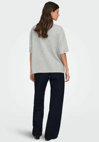 Szara, oversized koszulka z krótkim rękawem, wykonana z miękkiego materiału, zestawiona z ciemnoniebieskimi szerokimi spodniami dżinsowymi. Widok z tyłu ukazuje luźny krój i prosty design.