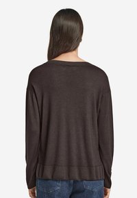 Brun oversized tröja med bred halsringning, ribbade ärmslut och fåll. Mjukt tyg, designad för en avslappnad passform. Bärs med blå jeans.